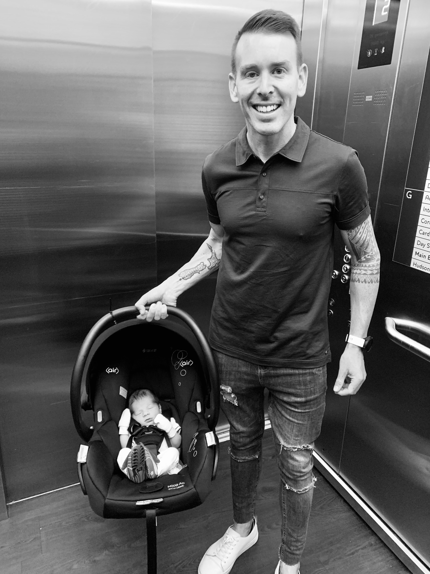 Philippe in an elevator with his newborn baby in a car seat, black and white