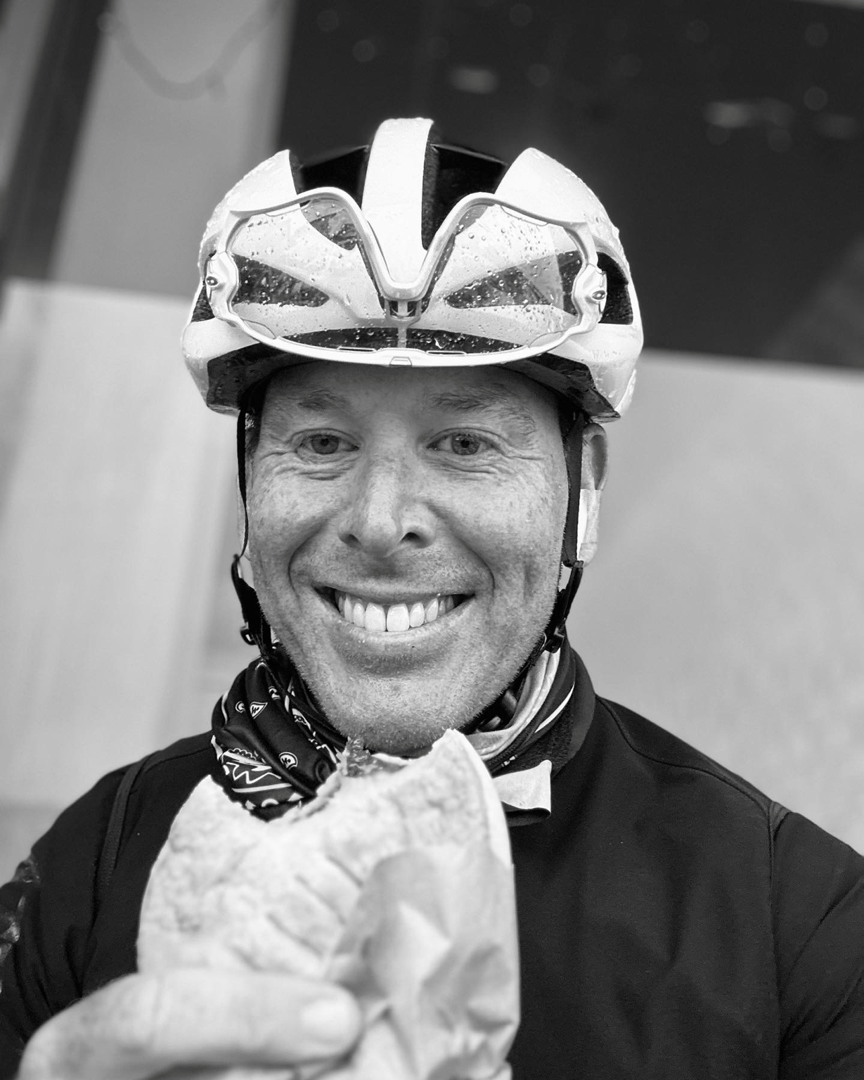Phillipe smiling in cycling kit after a ride, eating something wrapped in paper